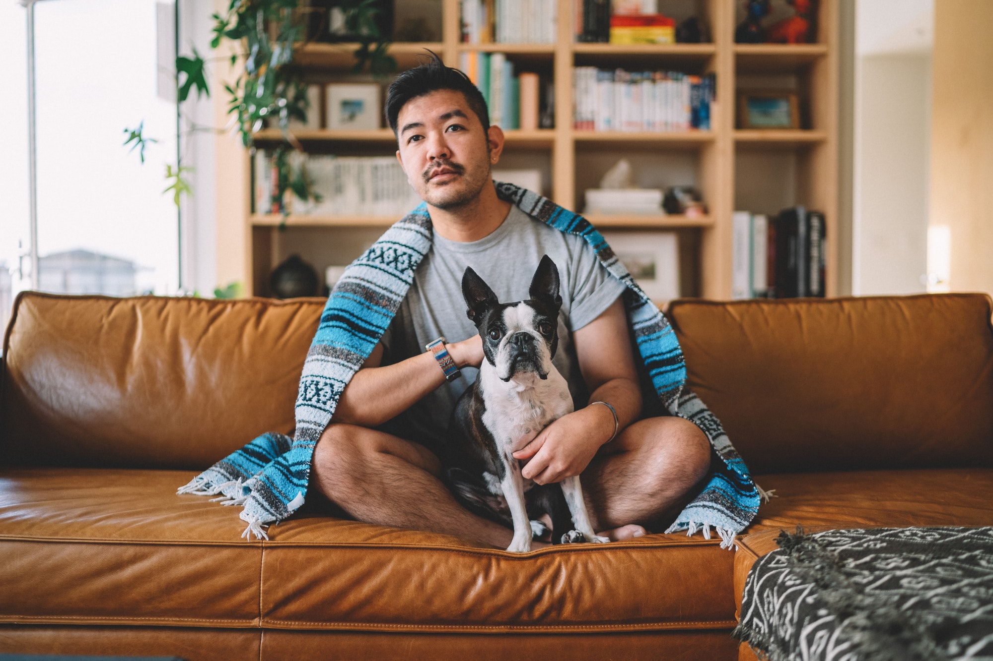 Guy sitting on couch, lounging with his dog watching TV with a blanket.